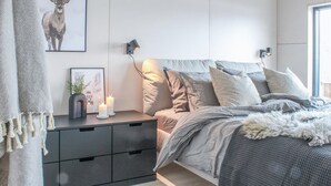 Une chambre à coucher avec un lit, des tables de chevet, une lampe fixée au mur et un tableau encadré.