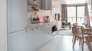 Une cuisine moderne avec des armoires blanches, un four encastré et un coin repas agrémenté de chaises et d’une table en osier.