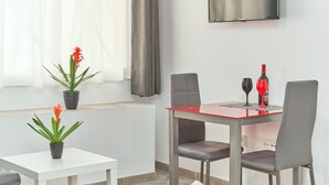 A modern dining area with a red table, grey chairs, a potted plant, and a TV mounted on the wall. - Studio Apartment "Nerja Boutique Street Level B1" with Shared Pool & Wi-Fi (Nerja)