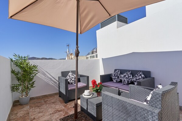 Un espace extérieur aménagé avec des meubles en osier, une plante en pot et un parasol beige.