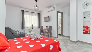 A modern hotel room with a bed, a desk, a chair, a TV, and a bathroom visible through an open door. - Studio Apartment "Nerja Boutique Street Level B1" with Shared Pool & Wi-Fi (Nerja)