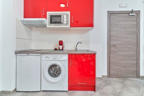 Une cuisine compacte équipée d’un lave-linge, d’un four à micro-ondes et d’un meuble rouge.
