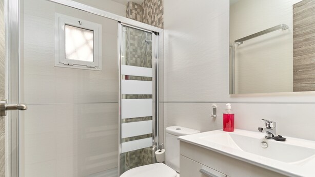 Een badkamer met douche, toilet, wastafel en spiegel.