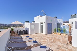 Une terrasse sur le toit, avec des chaises longues, une table avec des bouteilles et une vue sur le paysage.