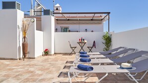 Una terraza en la azotea con sillones de descanso, una mesa y una planta en maceta.