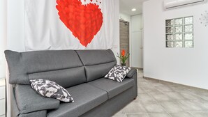 Un sofá gris con almohadones estampados, una pared con diseño de corazón rojo y un ventanal con vidrio satinado.