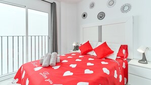 Un dormitorio con cama, almohadas, mesita de noche, lámpara y balcón.