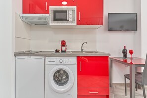 A compact kitchen with a washing machine, a microwave, and a TV.