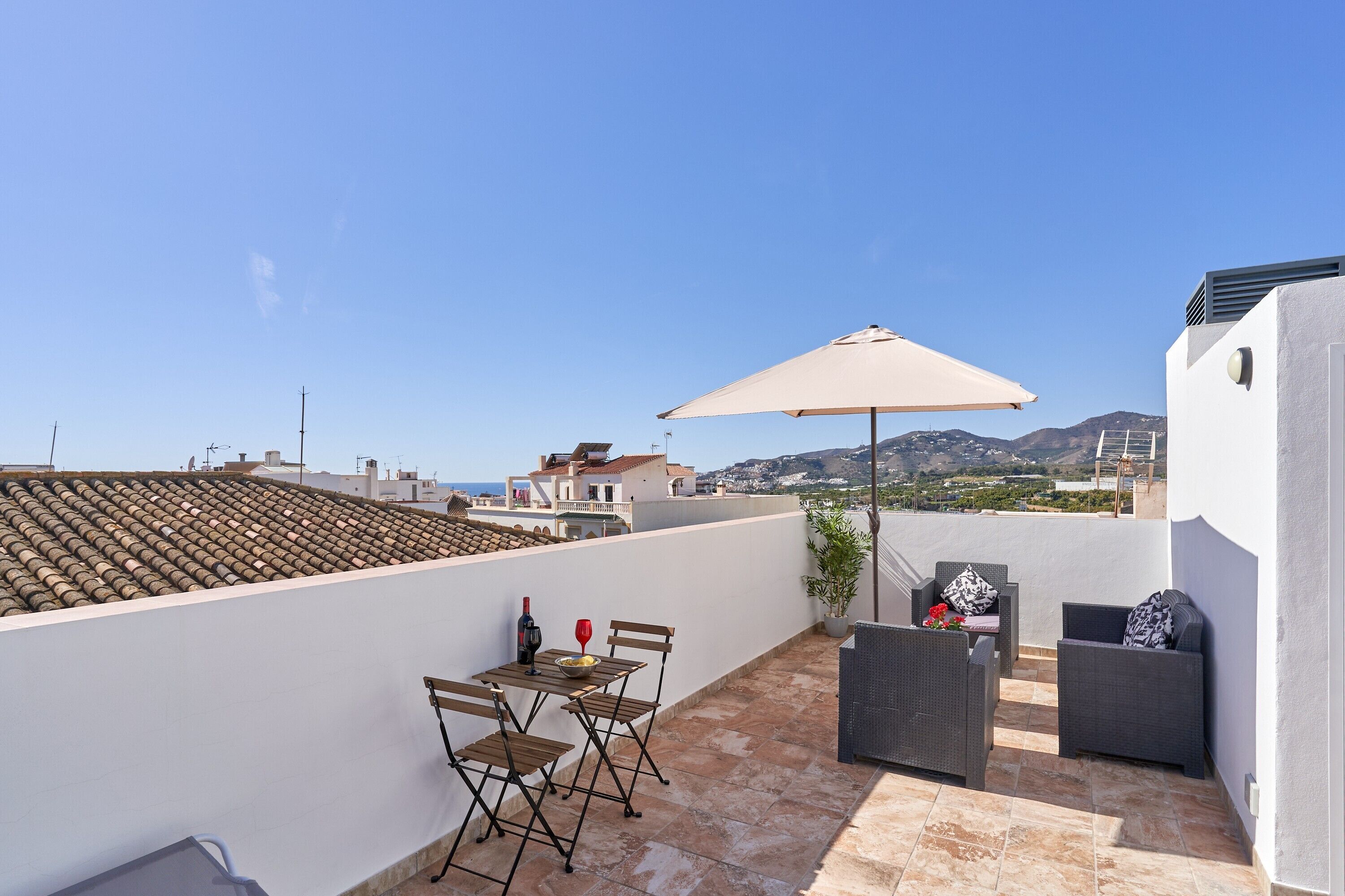 Une terrasse sur le toit, avec une table, des chaises, un grand parasol et un canapé.
