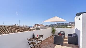 Une terrasse sur le toit, avec une table, des chaises, un grand parasol et un canapé.