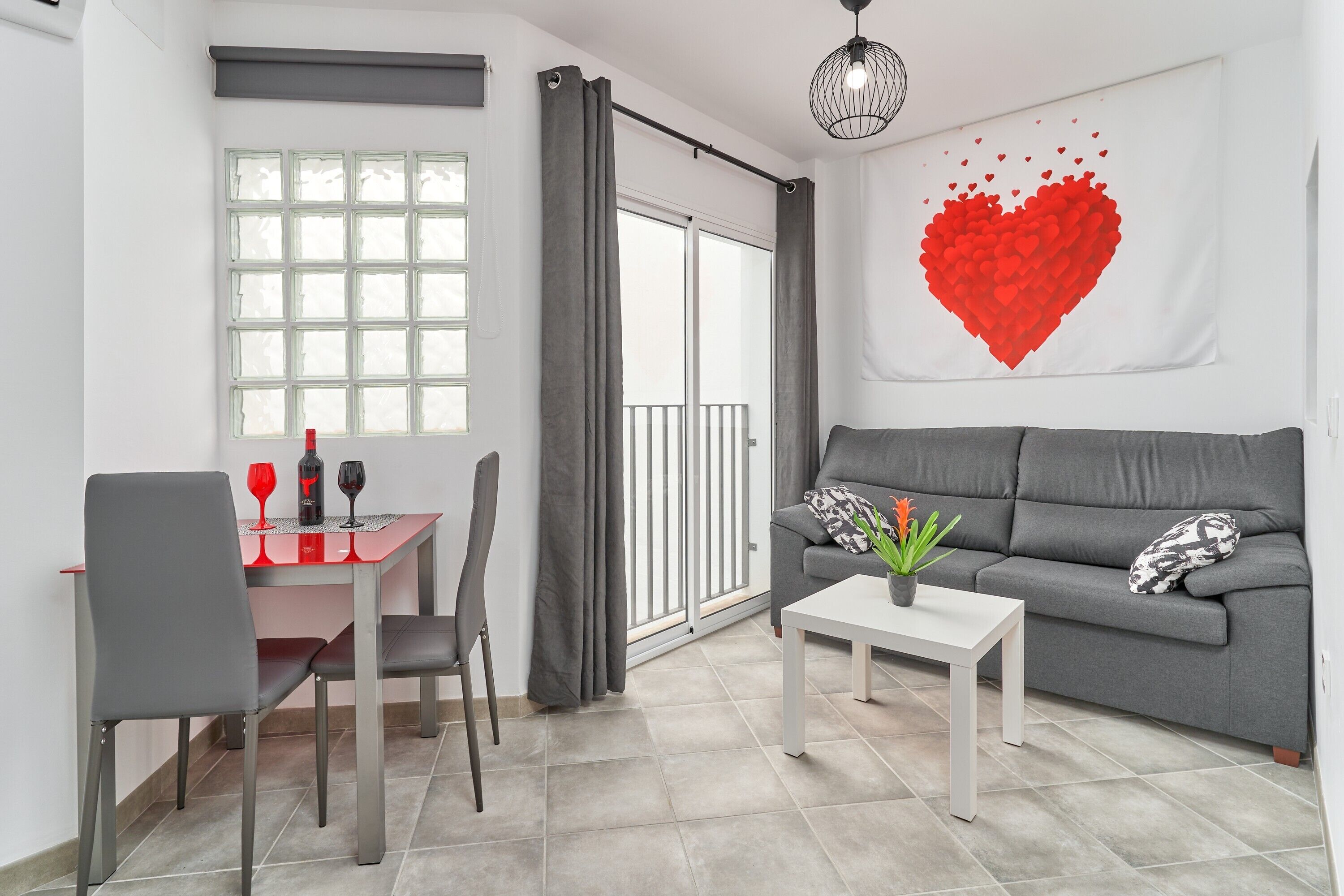 A modern living room with a grey sofa, a dining table with chairs, a white coffee table, and a large window with curtains.