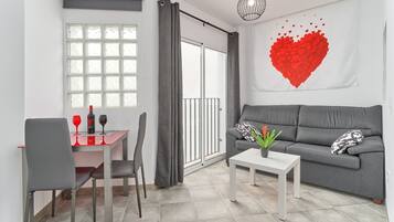 A modern living room with a grey sofa, a dining table with chairs, a white coffee table, and a large window with curtains.