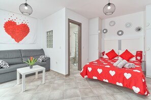 Une chambre moderne avec un lit, un canapé gris, une petite table et un mur décoratif en forme de cœur.