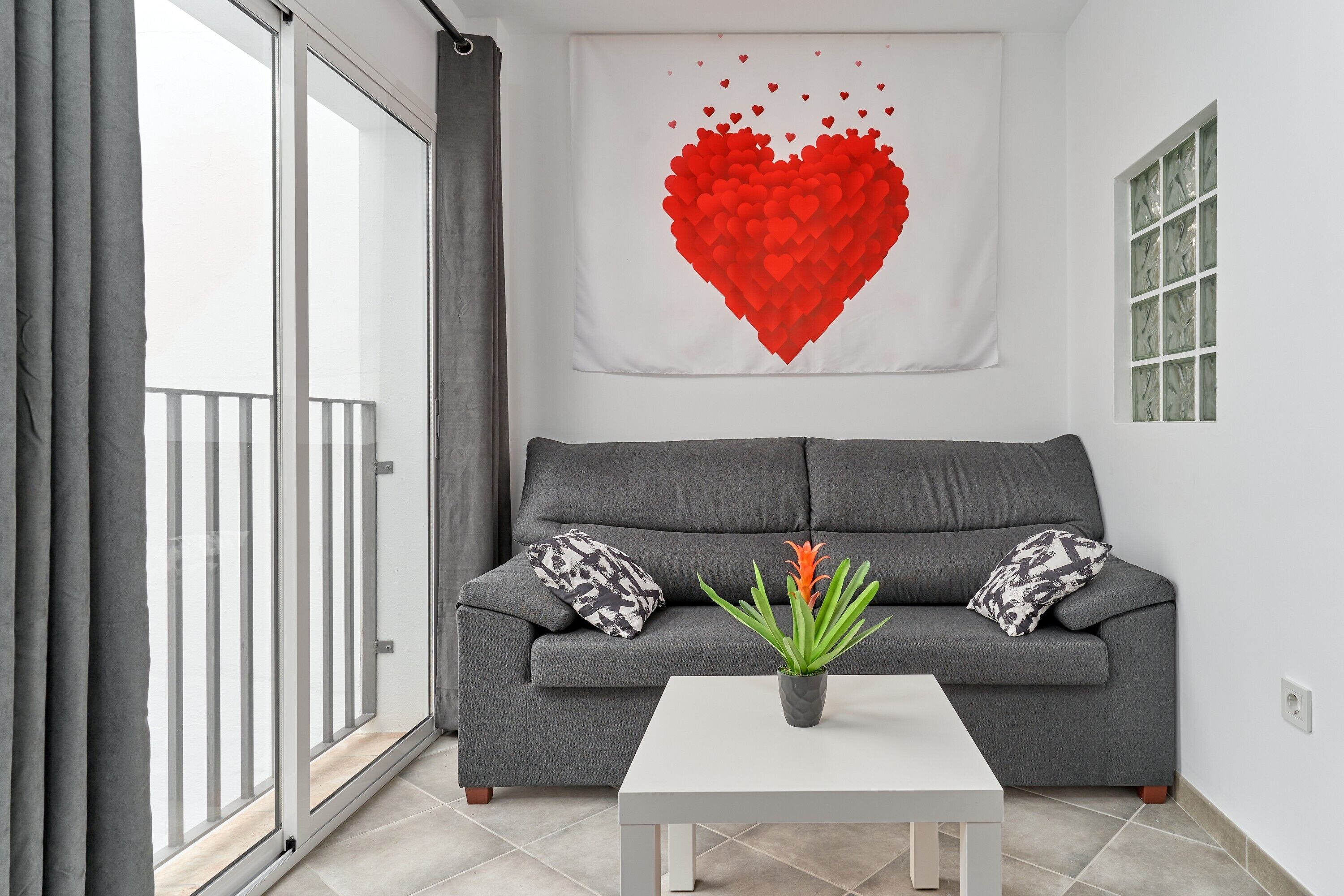 A living room with a grey sofa, a white coffee table, and a red heart artwork on the wall.