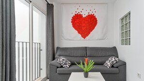 Una sala de estar con un sofá gris, una mesa de centro blanca y una obra de arte con forma de corazón rojo en la pared.