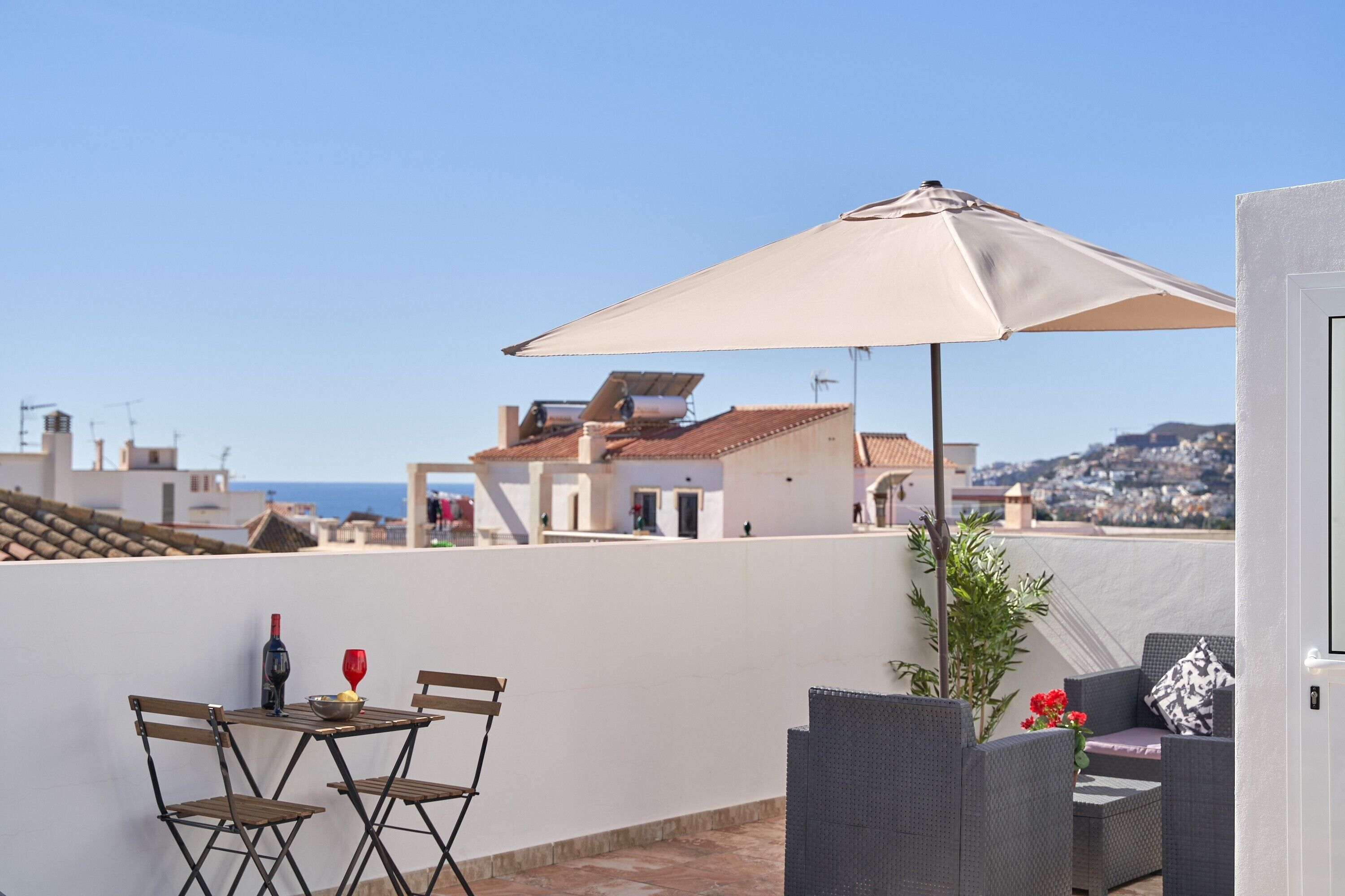 A rooftop terrace with a table, chairs, an umbrella, and a potted plant.