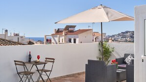 Una terraza en la azotea con mesa, sillas, una sombrilla y una planta en maceta.