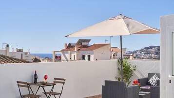 A rooftop terrace with a table, chairs, an umbrella, and a potted plant.