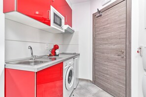 A compact kitchen with a washing machine, a microwave, and a red cabinet. - Studio Apartment "Nerja Boutique Sweet Corner B3" with Shared Pool & Wi-Fi (Nerja)