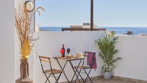 A terrace with a table, chairs, a potted plant, and a view of the sea.