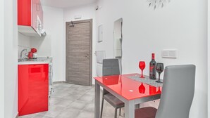 A compact kitchen with red cabinets, a dining table with two chairs, and a wall-mounted clock.