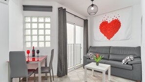 Un salon moderne avec un canapé gris, une table à manger avec des chaises, une table basse blanche et une grande fenêtre avec des rideaux.