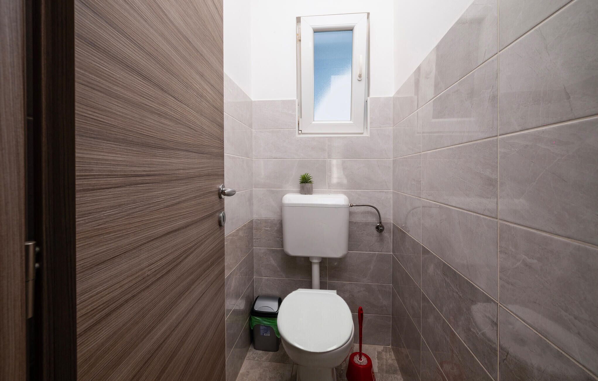 Un baño con inodoro, una ventana pequeña y una puerta.