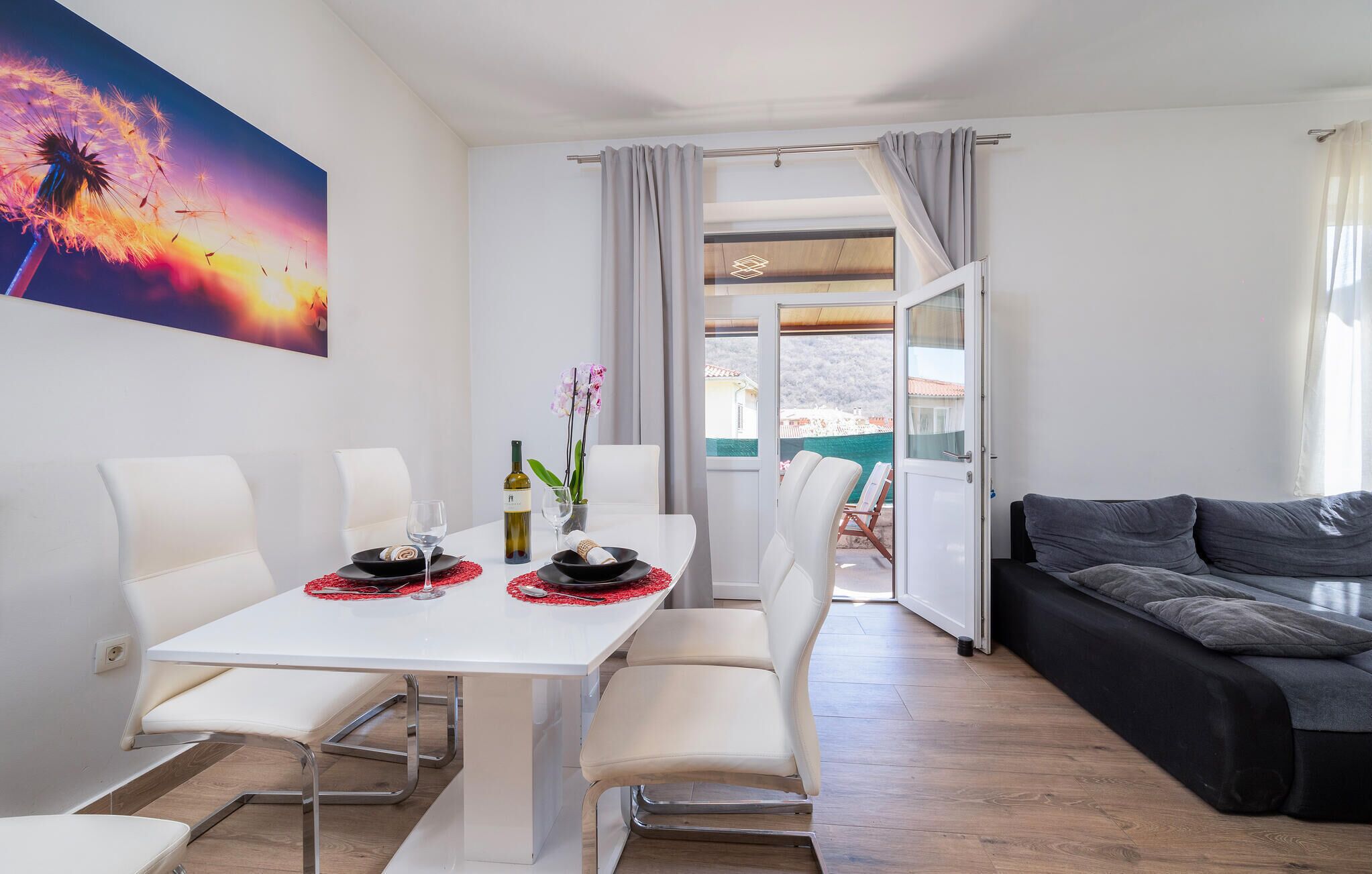 A modern living room with a white dining table, white chairs, and a black sofa.