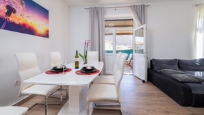 A modern living room with a white dining table, white chairs, and a black sofa.