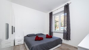 A bedroom with a bed, a wardrobe, a window with curtains, and a view of the outside.