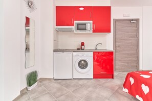 Une cuisine compacte équipée d’un four à micro-ondes, d’un lave-linge et de meubles de rangement rouges.