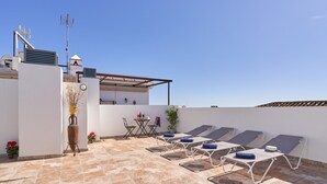 Une terrasse sur le toit, aménagée avec des chaises longues, une table et des plantes en pot.