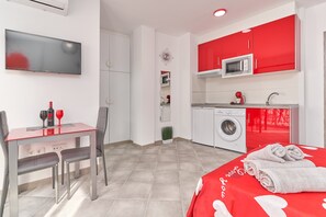 Une chambre d’hôtel moderne dotée d’un coin repas, d’une télévision, d’un lave-linge et d’une couvre-lit rouge.