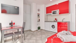 Een moderne hotelkamer met een zithoek, een televisie, een wasmachine en een rode sprei.