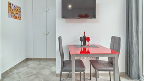 Ein Essbereich mit rotem Tisch, grauen Stühlen, einem an der Wand montierten Fernseher und einem Fenster mit Vorhängen.