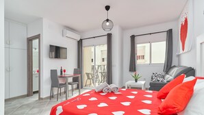 Ein modernes Schlafzimmer mit roter Bettdecke, einem Fernseher, einem Essbereich und einem Balkon.