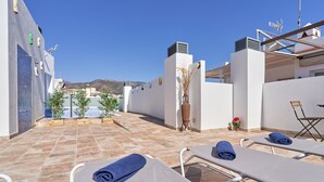 Eine Dachterrasse mit Liegestühlen, Blick auf das Meer und eine bergige Landschaft im Hintergrund.