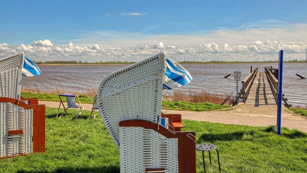 Un paisaje junto al lago con sillas de mimbre y una terraza de madera que se extiende sobre el agua.
