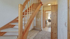 Una escalera de madera con barandilla que lleva a una habitación con suelo de baldosas y un banco.