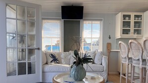 Un salón acogedor con un sofá blanco, una mesa de centro de mimbre y un jarrón, y vistas al mar a través de amplios ventanales.