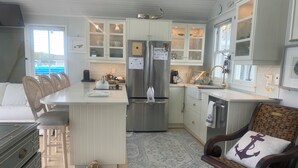 Una cocina con una isla central, armarios blancos y una zona de comedor con sillas de mimbre.