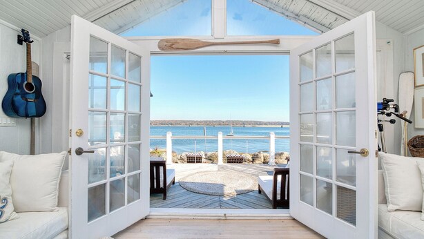 Puerta abierta que da a una terraza con vistas al mar, una guitarra y un interior rústico.