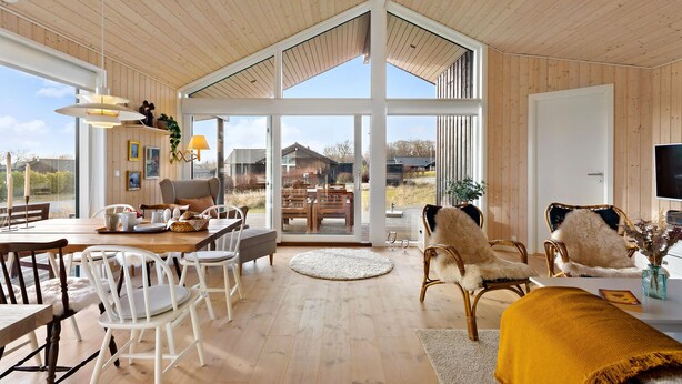 Amplia sala de estar con techo alto, paredes de madera y un gran ventanal corredero que da a una terraza exterior.