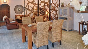 Een eetgedeelte met een houten tafel en rieten stoelen, omringd door een rustieke inrichting, waaronder een houten kast en een wandrad.