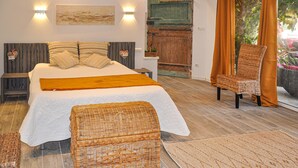 Een slaapkamer met een groot bed, een rieten stoel en uitzicht op het omliggende landschap.
