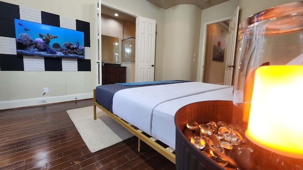 A bedroom with a bed, a TV on the wall, and a lit candle on a table. - Horizon House | Dual Home |Private Pool |Sleeps 16 (Houston)