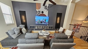 A modern living room with a sectional sofa, a coffee table, and a flat-screen TV mounted on the wall. - Horizon House | Dual Home |Private Pool |Sleeps 16 (Houston)