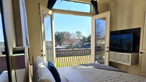 A bedroom with a large bed, an open sliding door to a balcony, and a TV mounted on the wall. - Horizon House | Dual Home |Private Pool |Sleeps 16 (Houston)