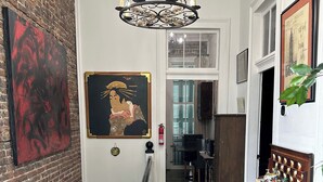 A hallway with a chandelier, a red abstract painting, a framed portrait, and a patterned rug. - Heart of Downtown w Balcony by Dauphin St; walk to restaurants & shops SLEEPS 6! (Mobile)