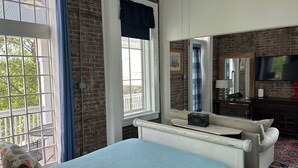 A bedroom with a bed, a sofa, a TV, and a brick wall. - Heart of Downtown w Balcony by Dauphin St; walk to restaurants & shops SLEEPS 6! (Mobile)